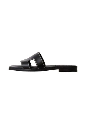 Sort flad slide-sandal med bred rem med udskårne detaljer og hvide syninger, vist fra siden på hvid baggrund.