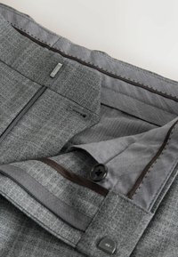 Tissu gris texturé avec un motif subtil, comprenant une fermeture métallique, deux boutons et une doublure intérieure contrastante. Conception ajustée avec poches.