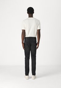 Černé džíny s úzkým střihem, s prostředně vysokým pasem a zadními kapsami. Doplněné jednoduchou bílou košilí s krátkým rukávem.