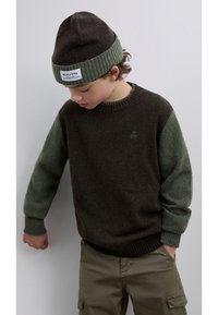 Tummanruskea ja vihreä neulepaita, jossa on resorit hihansuissa ja pieni vihreä pääkallologo. Yhdistetty oliivinvihreään pipoon.