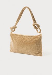 Zlata večerna torbica z okrasnimi kamenčki in zavezanim trakom, ki stoji na enobarvni svetlo sivi podlagi.