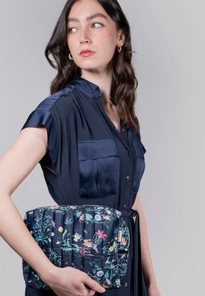 Borsa trapuntata blu navy con un motivo floreale che presenta vari colori. Tessuto liscio con una forma arrotondata, tenuta da una persona in un vestito scuro.