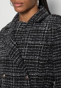 Cappotto a quadri bianco e nero in tessuto strutturato con collo a revers, design doppiopetto e bottoni color argento.