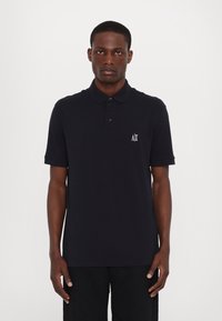 Marineblå polo skjorte laget av bomull, med krage, tre-knapps placket og en liten hvit brodert logo på brystet.