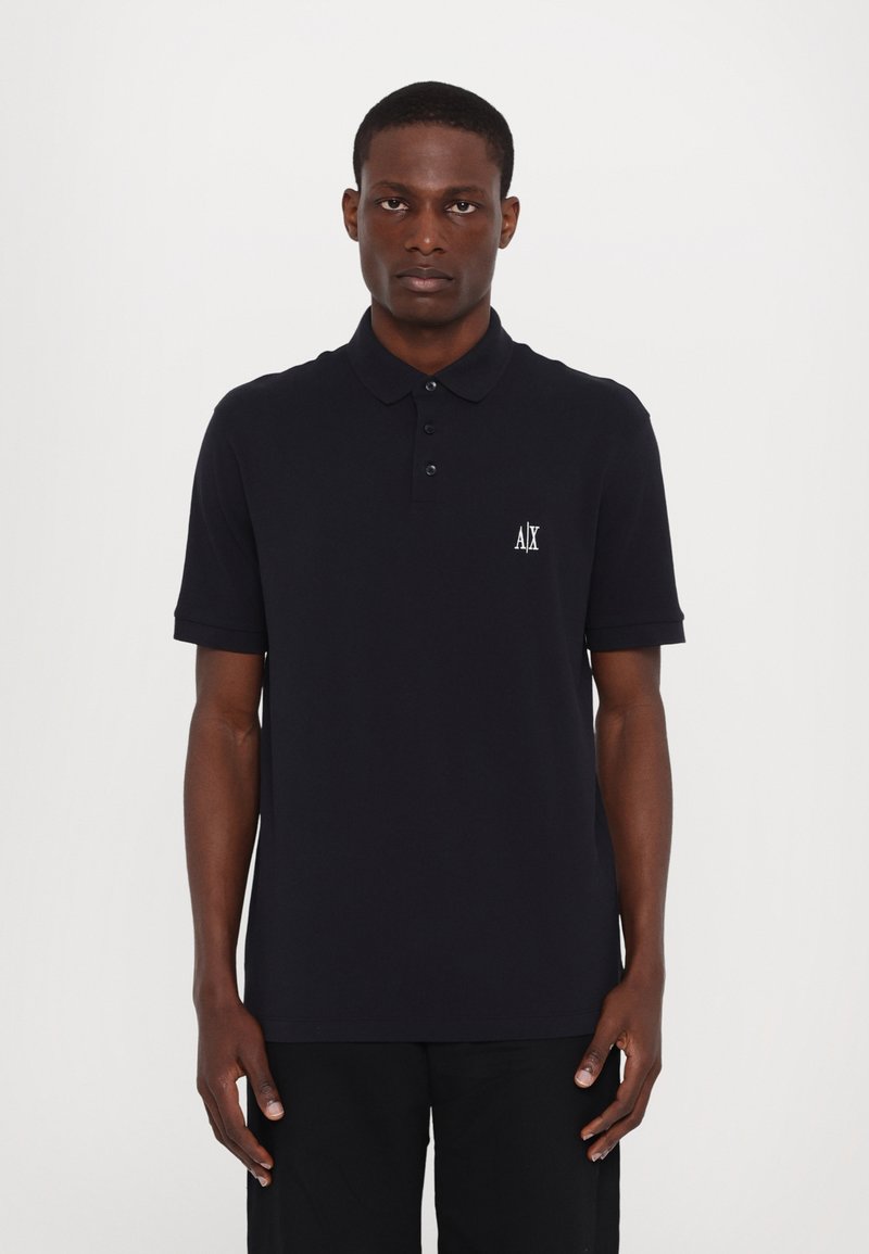 Marineblå polo skjorte laget av bomull, med krage, tre-knapps placket og en liten hvit brodert logo på brystet.