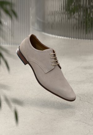 Beige suede dress shoe with a pointed toe, featuring light laces and a wooden heel. The surface is smooth with no visible patterns.
