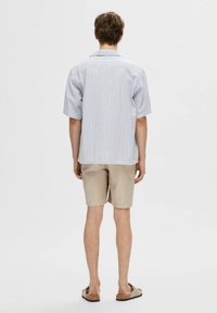 Jasnoniebieska koszula z krótkim rękawem z teksturowanym wzorem w paski, zestawiona z beżowymi szortami i brązowymi klapkami. Tło jest jednolicie białe.