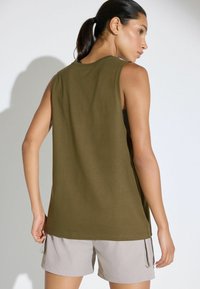 Canotta senza maniche verde oliva con vestibilità rilassata, realizzata in morbido cotone. Abbinata a pantaloni corti grigi chiari con tasche laterali.