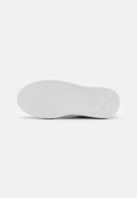 Bílá podrážka tenisky s texturovaným gripem, obsahující logo a mírný oblouk. Hladký gumový materiál s zaobleným podpatkem.