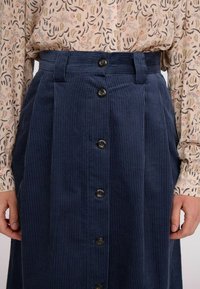 Sötétkék kordbársony szoknya függőleges csíkokkal, magas derékkal, két oldalzsebbel és hat fekete gombbal az elején.
