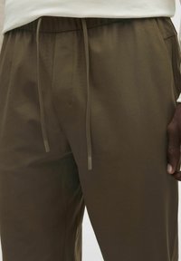 Brązowe spodnie elastyczne z wiązaniem w pasie. Gładka struktura i tapered design, z bocznymi kieszeniami i luźnym krojem.