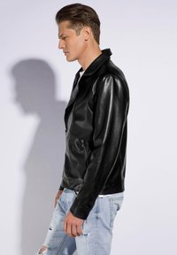 Schwarze Leder-Bikerjacke mit scharfem Kragen, Reißverschlusstaschen und tailliertem Schnitt, kombiniert mit hellblauen, distressed Jeans.