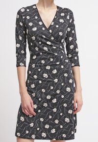 Zwarte wikkeljurk met een bloemenpatroon in het wit, met driekwart mouwen en een v-hals. Zacht materiaal met een mooie drape.