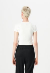 Kortermet hvit croppet t-skjorte laget av mykt stoff, kombinert med svarte bukser med elastisk liv. Rette linjer, enkelt design, sømløs tekstur.
