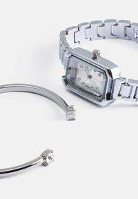 Relógio de pulso em tom prateado com mostrador retangular, marcadores de cristal e uma pulseira de metal. Inclui uma pulseira de pulso curvada em prata separada com um detalhe em gema.