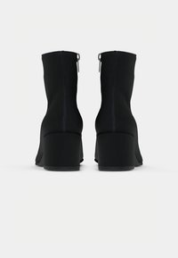 Botas de tornozelo pretas com um design justo, salto alto em bloco e detalhe em zíper na parte traseira. O material parece liso com um acabamento mate.
