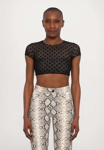 Crop top noir à manches courtes, avec un mesh texturé et un motif à pois, associé à un pantalon taille haute à imprimé serpent beige et gris.