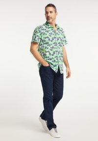 Koszula z krótkim rękawem z zapięciem na guziki, z zielonym i białym nadrukiem tropikalnych liści. Połączona z ciemnoniebieskimi dżinsami i białymi trampkami.
