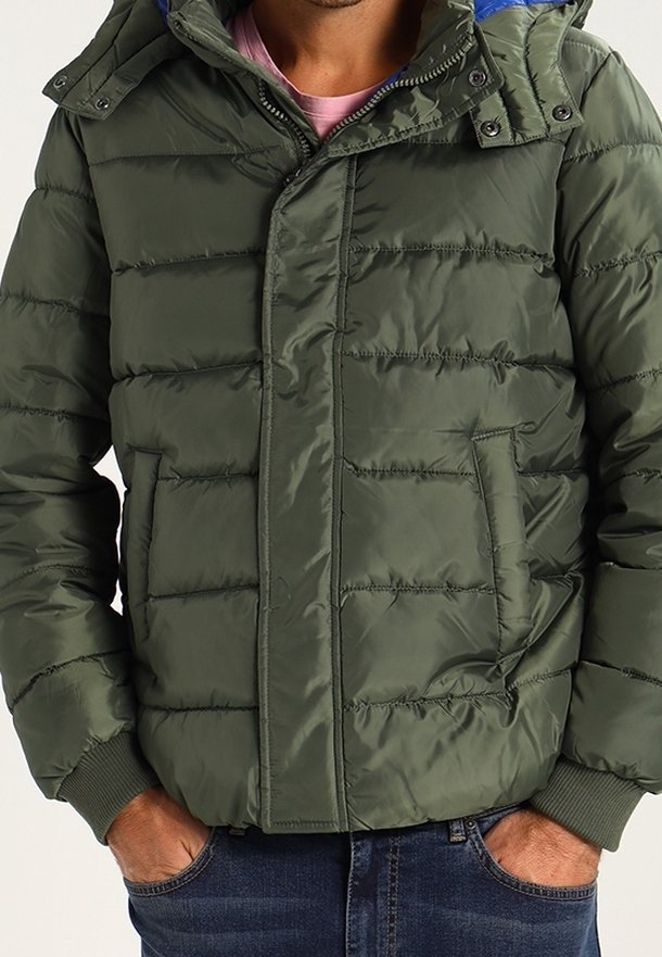 Grön puffjacka med framdragkedja, huva och ribbade ärmar. Har horisontell sömnad och två sidofickor.