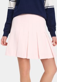 Light pink pleated skirt with a smooth texture, featuring crisp pleats and a mid-length cut, paired with a navy sweater.