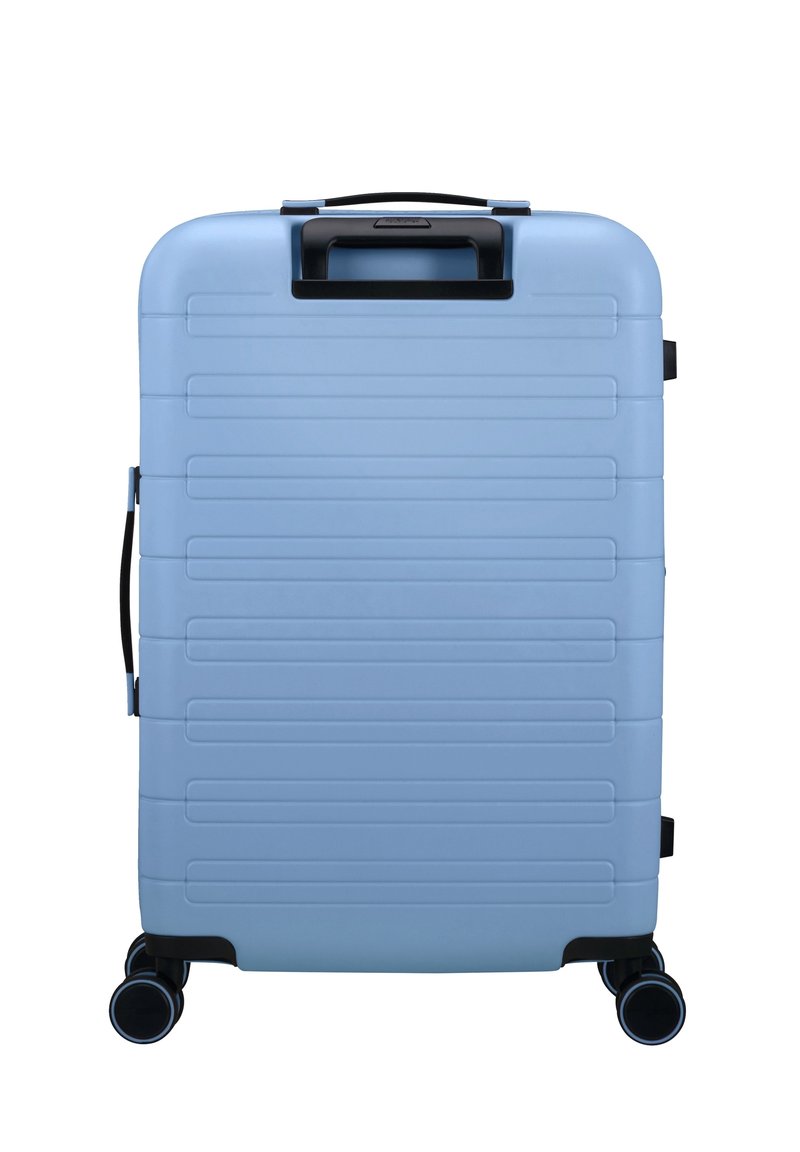 Valigia rigida di colore azzurro chiaro con scanalature verticali, manico superiore, manico laterale e quattro ruote nere per la mobilità.