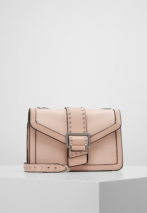 Sac bandoulière rectangulaire rose clair avec des clous argentés, une grande boucle centrale et une sangle amovible posée sur une surface blanche.