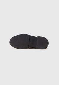 Suela de zapato de goma texturizada negra con un ligero tacón, fotografiada sobre un fondo blanco liso.