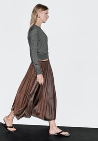 Šedý top s dlouhým rukávem v kombinaci s hnědou, vzdušnou saténovou maxi sukní. Modelka má na nohou černé žabky. Jednoduchý, elegantní střih.