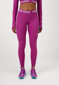 Fuksjowe legginsy z wysokim stanem z napisem "NIKE PRO". Noszone z pasującymi fuksjowymi butami, podkreślającymi bezszwowy sportowy design.