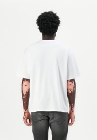 Camiseta de algodón blanca con un corte relajado, mangas cortas y un cuello redondo, combinada con jeans de color gris oscuro. Diseño sencillo sin patrones.