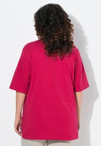 T-shirt a maniche corte in cotone rosa brillante, caratterizzato da una vestibilità ampia con orlo arrotondato e spacchi laterali per facilitare il movimento.
