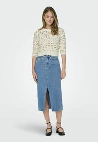 Witte gebreide trui met een open patroon, gecombineerd met een lichtblauwe denim midi-rok met een voorkapsluiting. Zwarte sandalen met banden maken de look compleet.