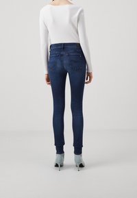 Jeans ajustados de denim azul oscuro con cintura alta, combinados con una camiseta blanca ajustada de canalé. Presentan bolsillos traseros y una silueta elegante.