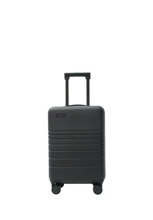 Czarna twarda walizka na kółkach z wysuwanym uchwytem, stojąca pionowo na białym tle.