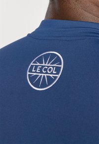 Maillot de cyclisme bleu marine au design ajusté, avec un logo circulaire blanc brodé Le Col dans le dos. Texture lisse.