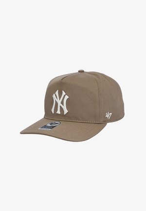 Beige baseball cap with white embroidered "NY" logo on front and "47" logo on side, featuring a curved brim and adjustable strap.