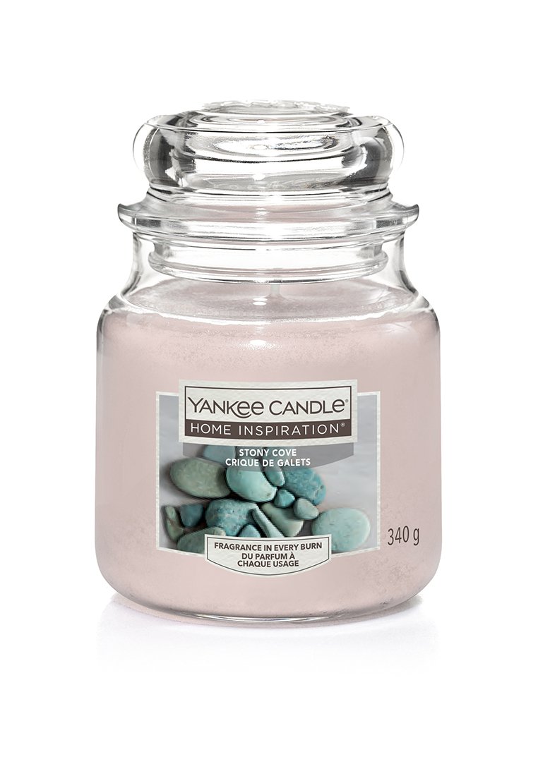 Candela in vaso di vetro rosa con coperchio trasparente, dotata di un'etichetta che mostra pietre teal e testo. Contiene 340 grammi di cera profumata.