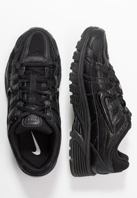 Czarne buty sportowe wykonane z siateczki i materiału syntetycznego, z teksturowaną powierzchnią, ze sznurowadłami i charakterystycznym wzorem podeszwy.