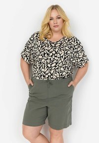Svart- och beige-mönstrad kortärmad topp kombinerad med gröna shorts med dragsko. Toppens passform är lös; shortsen är avslappnade och knälånga.