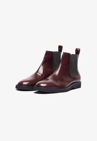 Bocanci Chelsea din piele bordeaux, cu panouri elastice laterale și tablă de încălțare, având un finisaj elegant, lucios și tălpi negre ușor texturate.