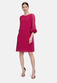 Fuchsia Kleid mit durchsichtigen Ärmeln, Rüschensaum und rundem Ausschnitt. Der Stoff hat eine glatte Textur, fließendes Design und endet knielang.
