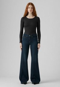 Un bodysuit noir à manches longues associé à un jean en denim bleu foncé à jambes larges. Le jean présente une taille haute et des détails de couture subtils.