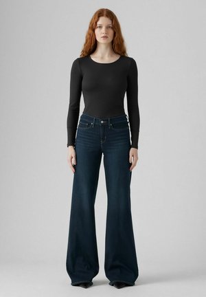 Zwarte longsleeve bodysuit gecombineerd met brede, donkerblauwe denim jeans. De jeans hebben een hoge taille en subtiele stikseldetails.