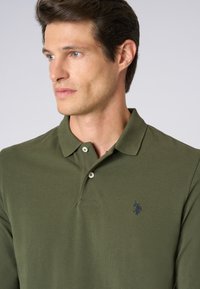 Polo shirt verde khaki in tessuto texture, con patta a tre bottoni e un piccolo logo ricamato sul petto.