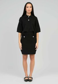 Ensemble en tricot noir en deux pièces comprenant un haut à manches courtes avec un col et des accents de boutons en perles, associé à une jupe ajustée.