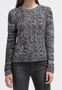 Maglione lavorato a maglia in bianco e nero con un design a treccia testurizzato e colletto rotondo. Maniche lunghe e orlo aderente. Tessuto testurizzato.