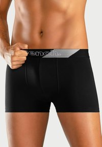 Schwarze Boxer-Briefs aus einem glatten Stoff, mit einem grauen elastischen Bund, auf dem der Markenname "Bench." in schwarzer Schrift gedruckt ist.