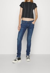 Camiseta negra recortada con costuras blancas, combinada con jeans ajustados azul oscuro y zapatillas de lona en blanco y negro. Look limpio y moderno.