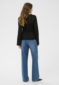 Sort blondelangeærmet top parret med løse lys blå denimjeans. Toppen har en mønstret tekstur og en tætsiddende silhuet.