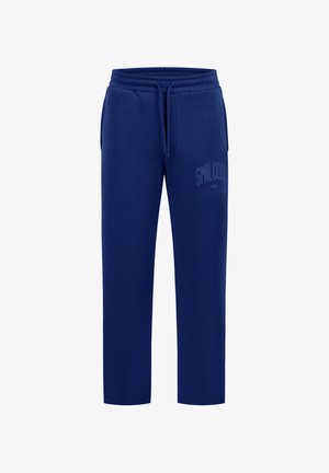 Pantalon de survêtement bleu marine avec taille élastique, cordon, poches latérales et détail textuel subtil sur la partie supérieure de la jambe gauche.